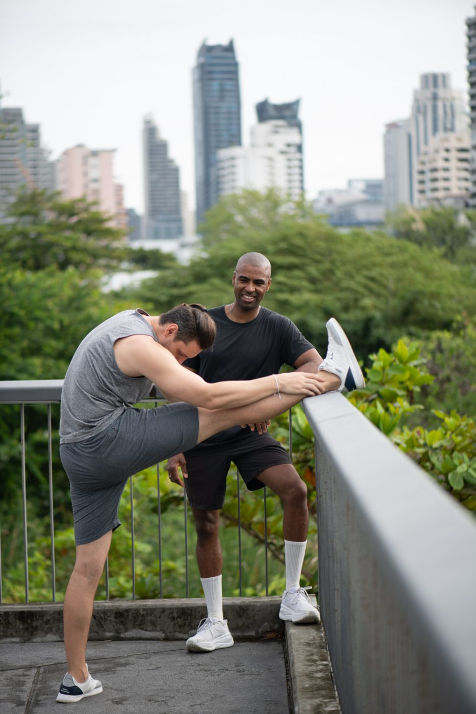 Jonathan Colorado coaching a client through a standing stretch outdoors with the New York City skyline behind them